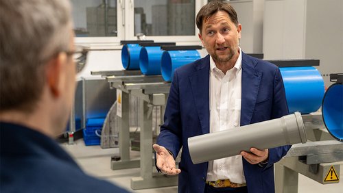 Ein Mann blickt in die Kamera und hält ein graues Rohr in der Hand