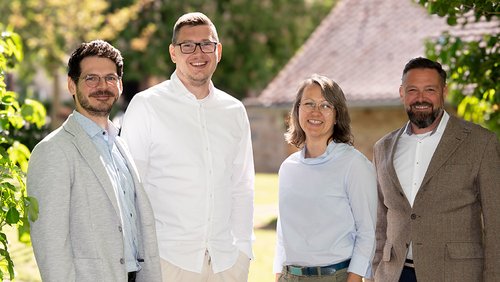 Gruppenbild von vier Personen auf einer Wiese bei Sonnenschein