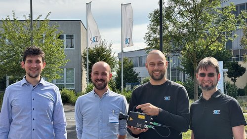 Vier Männer stehen draußen vor dem SKZ mit einem Prüfgerät in der Hand