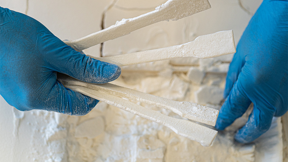 Zwei Hände mit blauen Gummihandschuhen halten weiße Zugstäbe aus Kunststoff